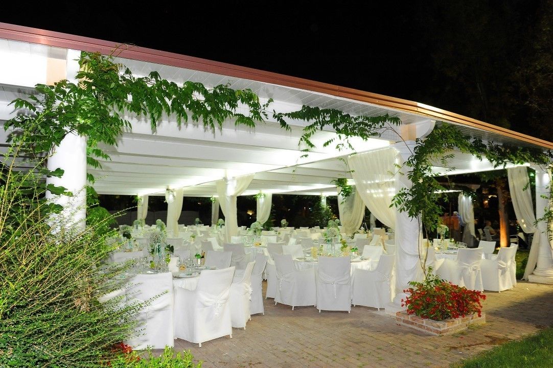 An outdoor event space with white tablecloths, chairs, and a covered area with draped fabric.