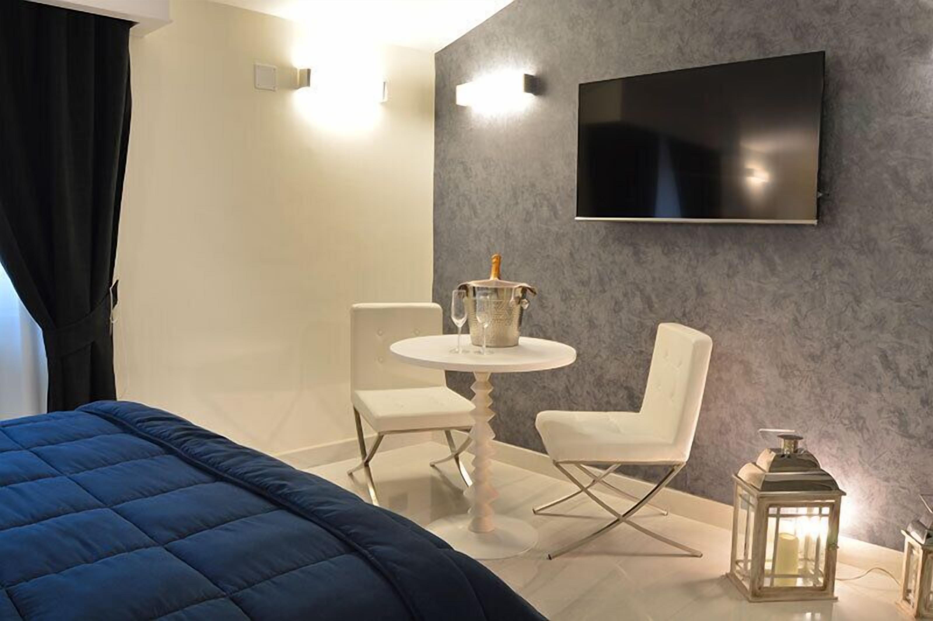 Una habitación de hotel moderna con una cama, una pequeña mesa redonda con dos sillas, un televisor montado en la pared y un farol decorativo.