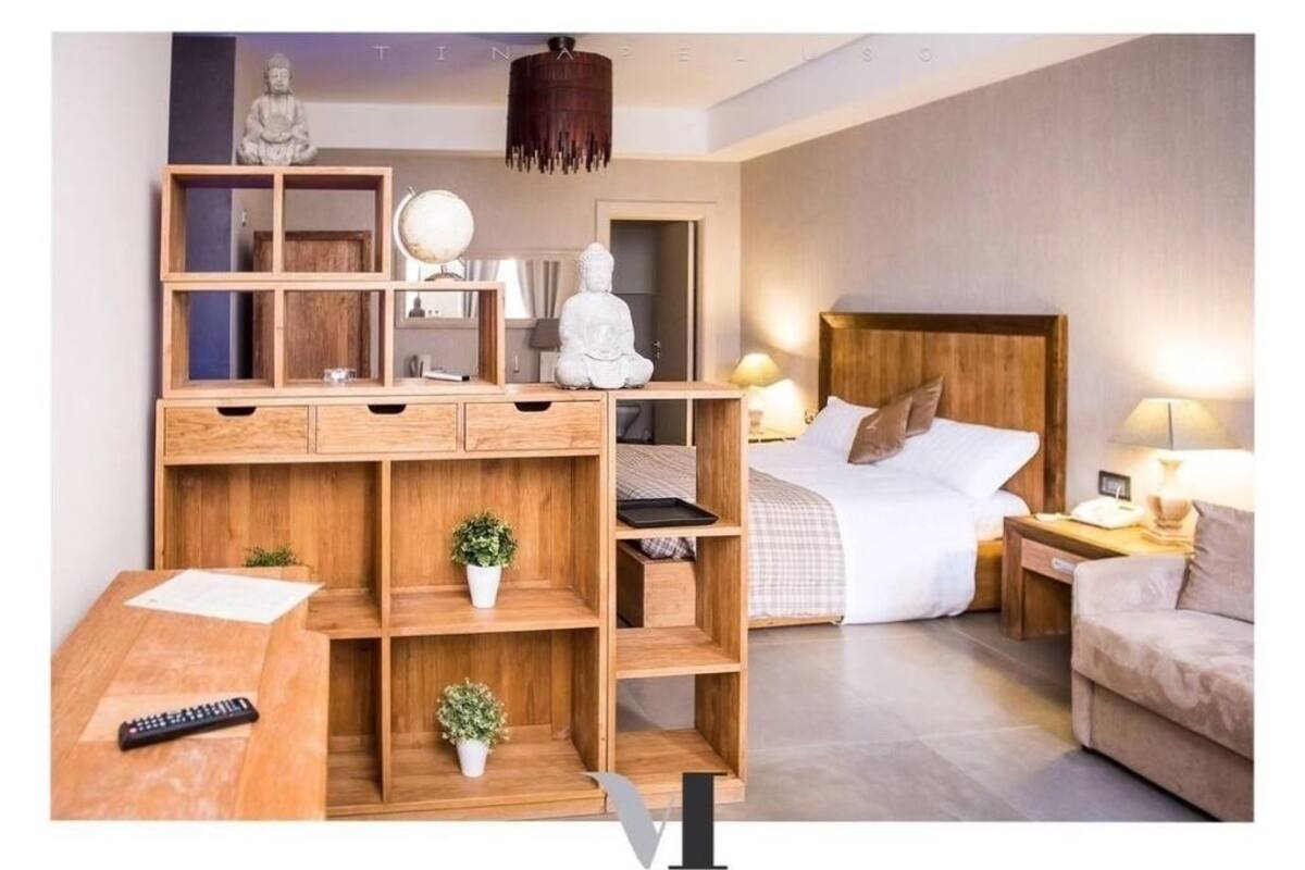 Quarto moderno com escrivaninha de madeira, cama com cabeceira de madeira, mesas de cabeceira com luminárias e uma estátua de Buda.