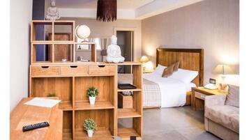 Une chambre moderne avec un bureau en bois, un lit avec une tête de lit en bois, des tables de chevet avec des lampes et une statue de Bouddha.