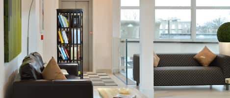 A modern living room with a black leather sofa, a wooden coffee table, and a bookshelf.
