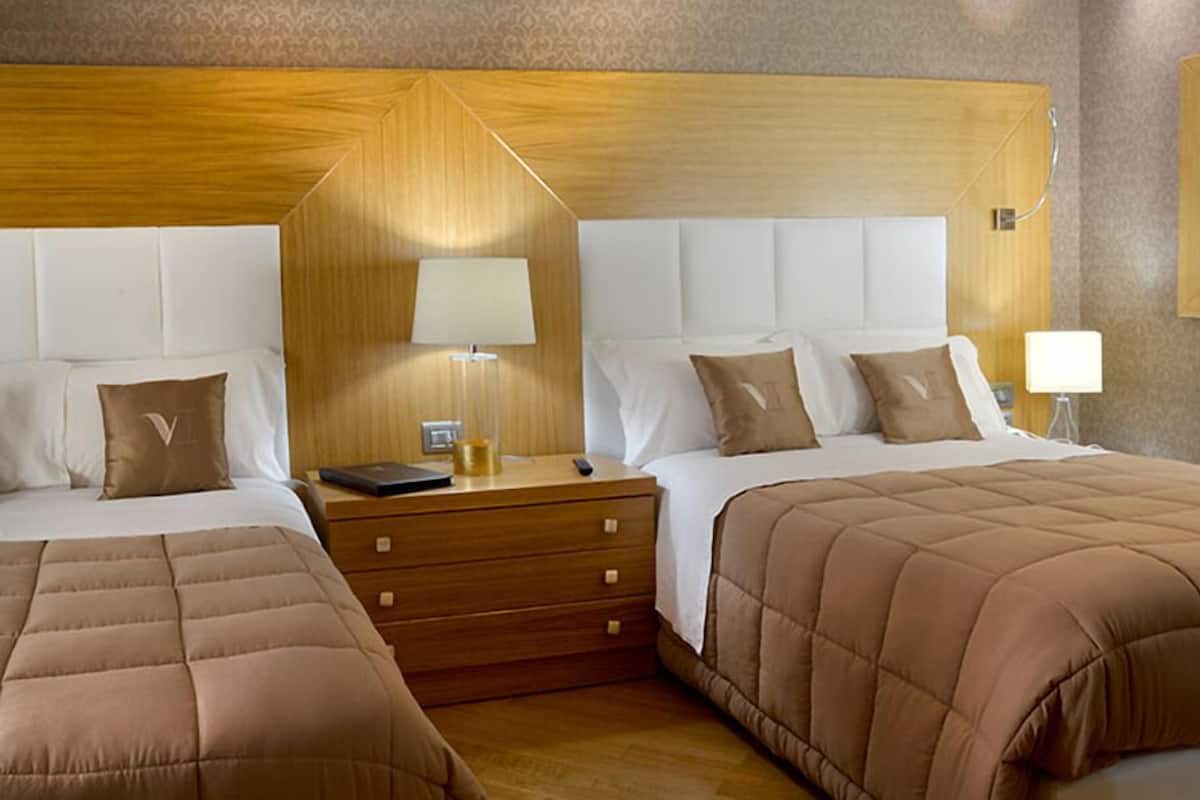 Quarto de hotel com duas camas, cabeceiras de madeira, mesas de cabeceira com abajures e um espelho na parede.
