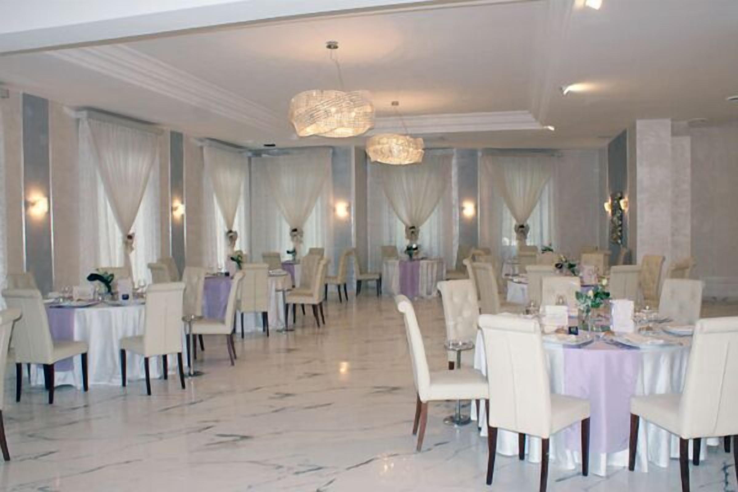 Un comedor amplio con varias mesas redondas, cada una con mantel blanco y sillas.