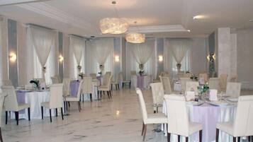 Un comedor amplio con varias mesas redondas, cada una con mantel blanco y sillas.