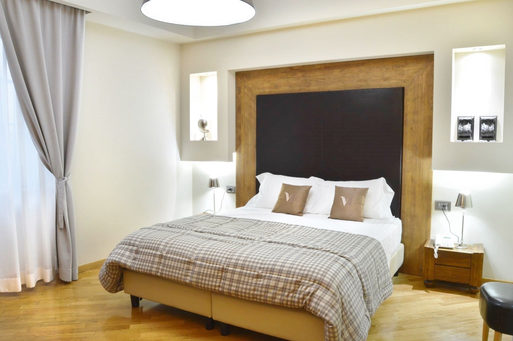 A bedroom with a large bed, a wooden headboard, a bedside table with a lamp, and a window with curtains.