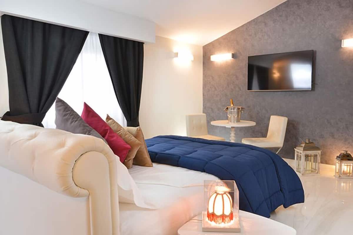 Quarto moderno com uma cama grande, uma TV na parede e uma mesinha com uma bebida.