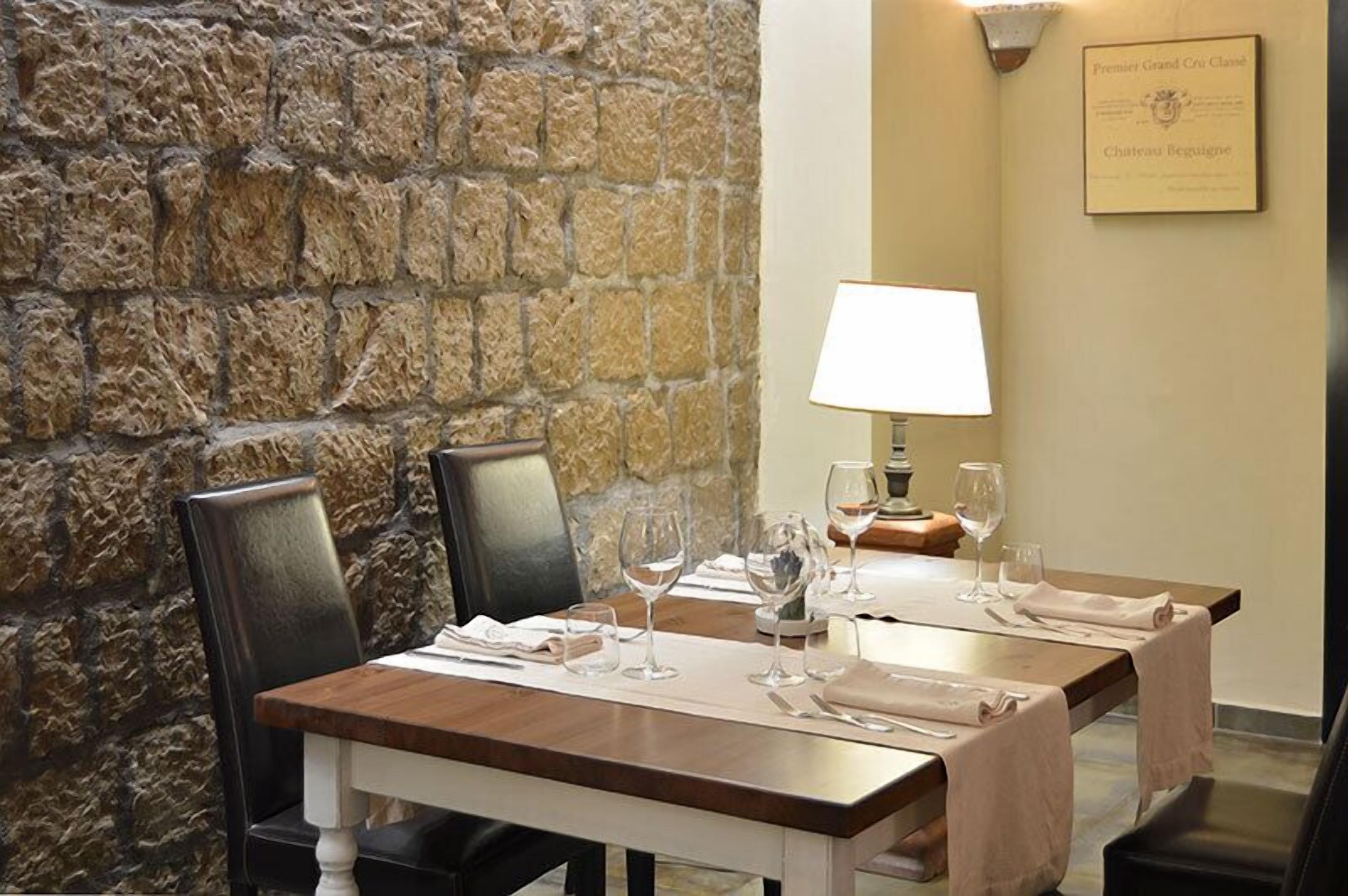 Un comedor con paredes de piedra, una mesa dispuesta con copas de vino y servilletas, y una placa en la pared.