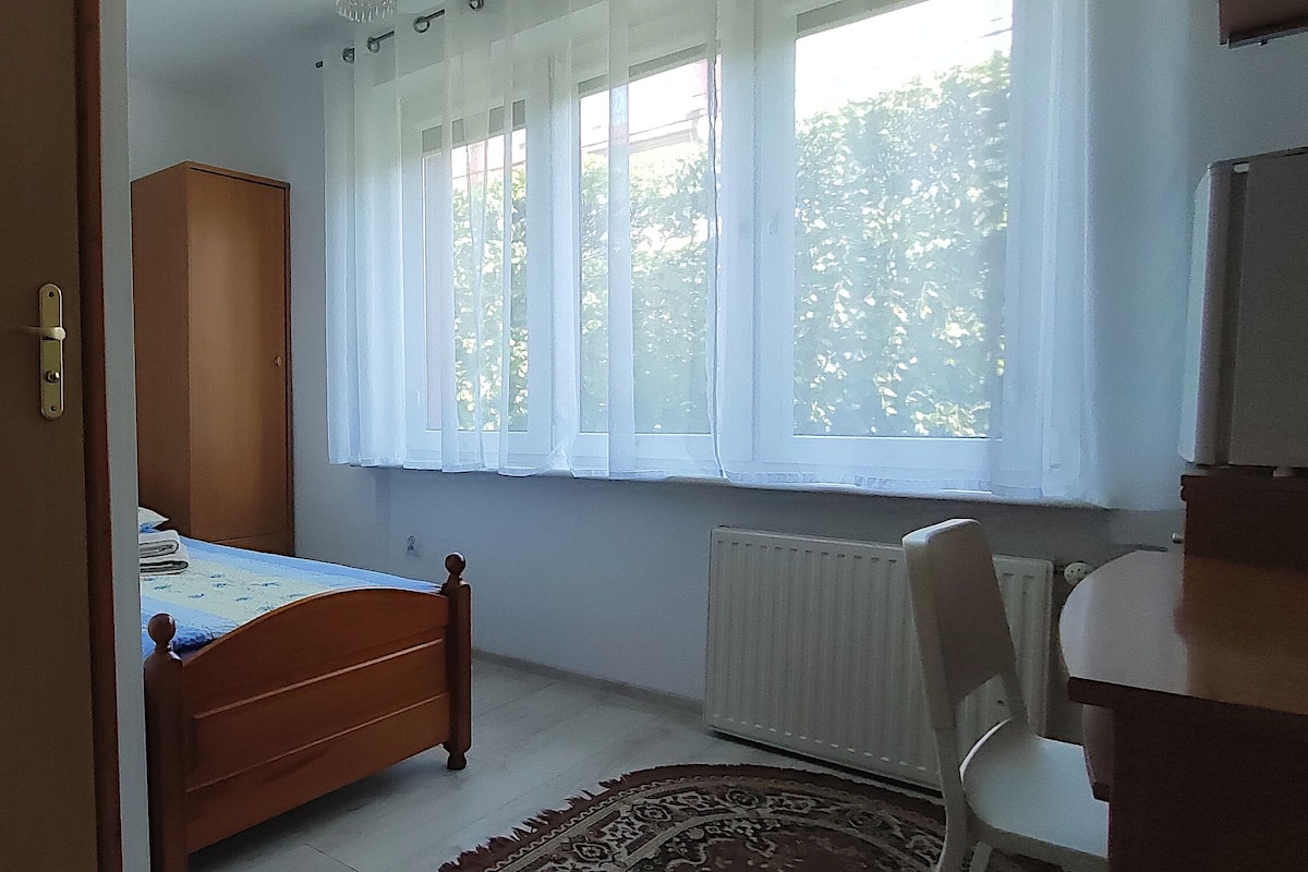 Un dormitorio con cama de madera, armario, radiador y ventana con cortinas.