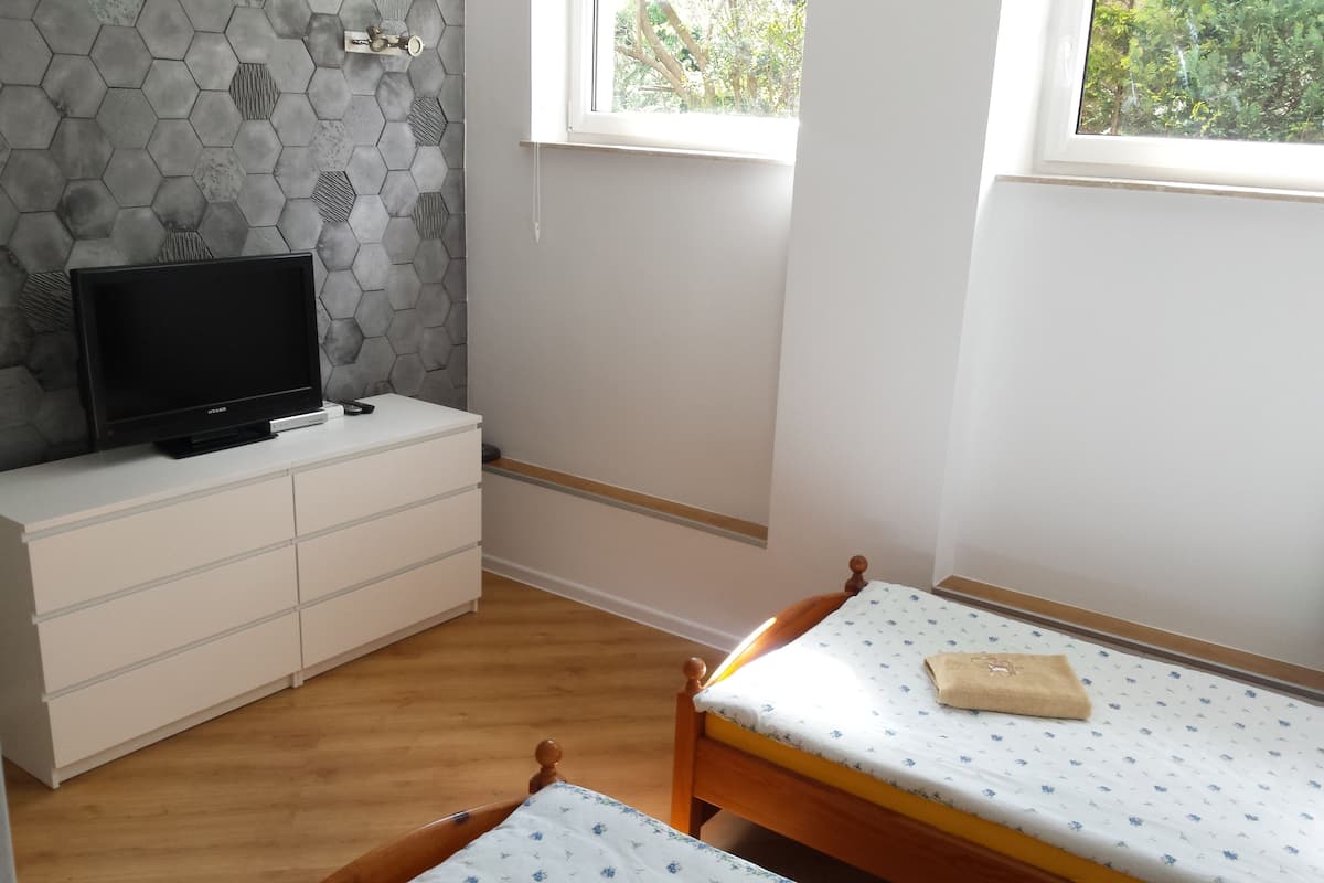 Un dormitorio con dos camas de madera, un tocador blanco, un televisor encima y una pared con diseño hexagonal.