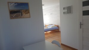 A bedroom with a wooden floor, a bed with a blue bedspread, and a small table with a chair.