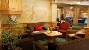 A cozy lounge area with a sofa, armchairs, a small table with drinks, and a wall mural.