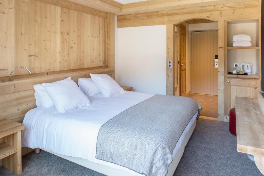 Ein Zimmer mit Holzboden, einem Bett, einem kleinen Tisch, einem Regal mit Handtüchern und einer Tür zu einem anderen Raum.