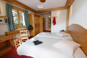 Habitación de hotel con una cama grande, cabecera de madera, un escritorio con silla, una ventana con cortinas y una toalla roja colgada en la pared.