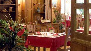 A dining area with a wooden table set for a meal, surrounded by wooden chairs and a red tablecloth.