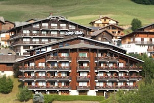 A multi-story hotel with balconies, a sign reading 'Hotel Club,' and a mountainous backdrop.