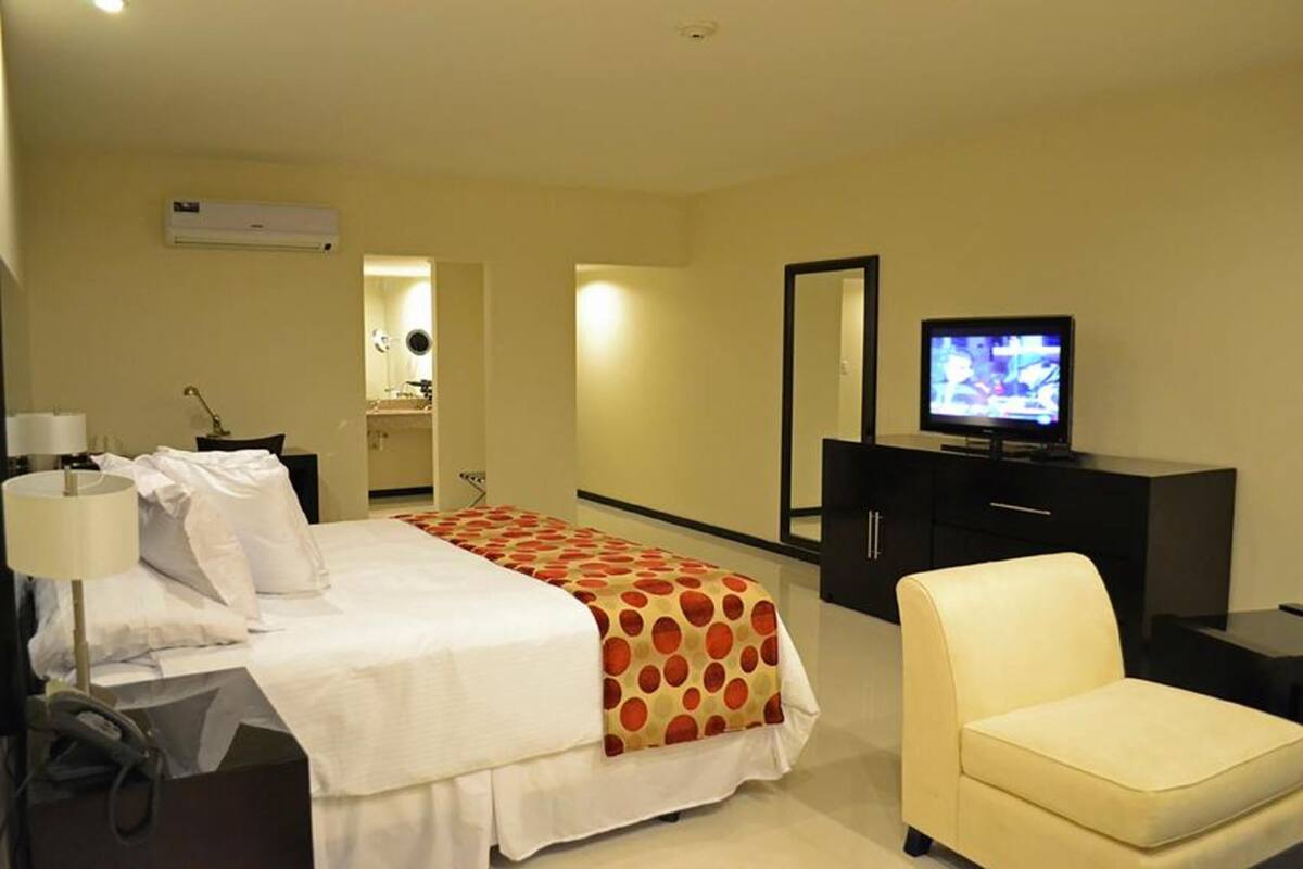 A hotel room with a bed, a television, a chair, and a desk with a lamp.