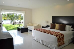 A modern hotel room with a large bed, a sofa, a desk, and a view of a pool and greenery. - Sun Hotel (Santa Cruz)
