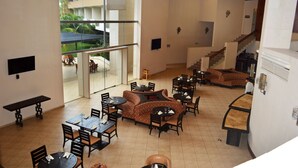 A spacious indoor area with multiple dining tables and chairs, a staircase, and large windows offering a view of the outdoors.