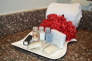 A tray with toiletries on a granite countertop, a white towel, and a bouquet of red flowers.