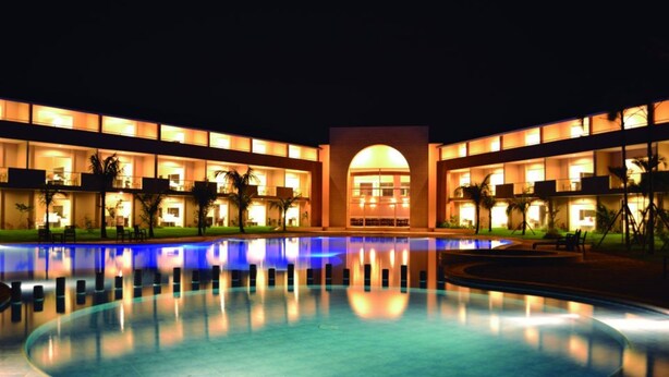 A hotel with a large swimming pool, multiple balconies, and a central arched entrance.