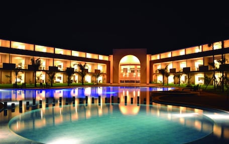 A hotel with a large swimming pool, multiple balconies, and a central arched entrance.