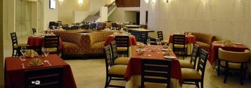 A dining area with round tables and chairs, a staircase in the background, and a carpeted floor.