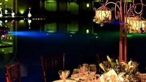 A table set for a meal with a view of a body of water and decorative lighting.