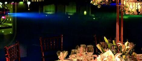 A table set for a meal with a view of a body of water and decorative lighting.
