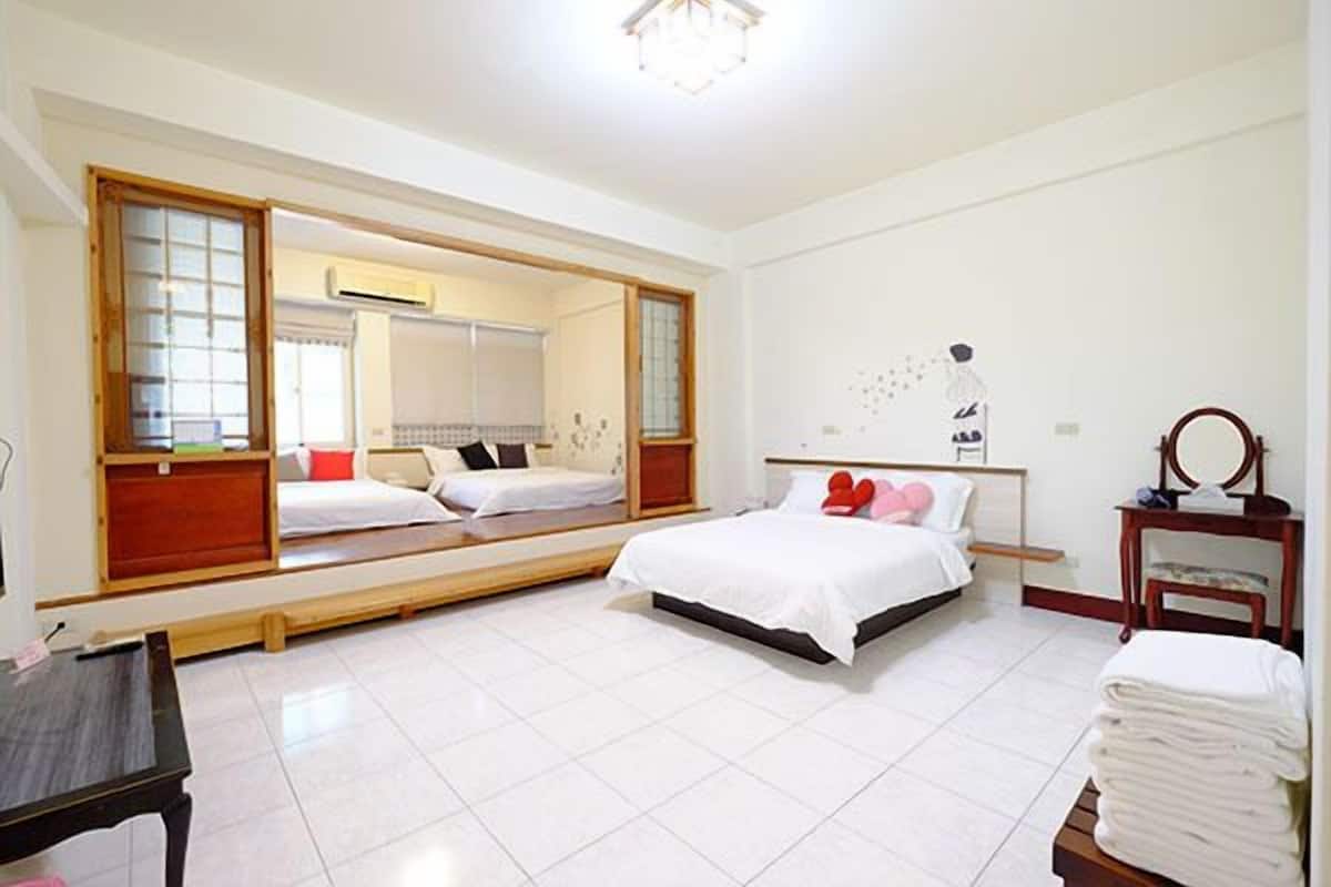 A hotel room with a large mirror, a bed with white bedding, a bedside table, and a chair.