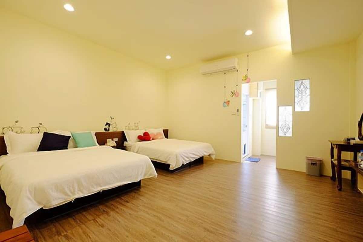 A bedroom with two beds, wooden flooring, and a visible door leading to another room.