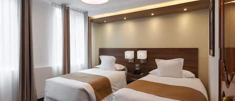 Habitación de hotel con dos camas, cabecero de madera, mesita de noche y una lámpara colgante moderna.