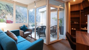 Un salon moderne comprenant un canapé, des fauteuils, une table en bois et une porte vitrée donnant sur un balcon aménagé avec du mobilier d’extérieur.