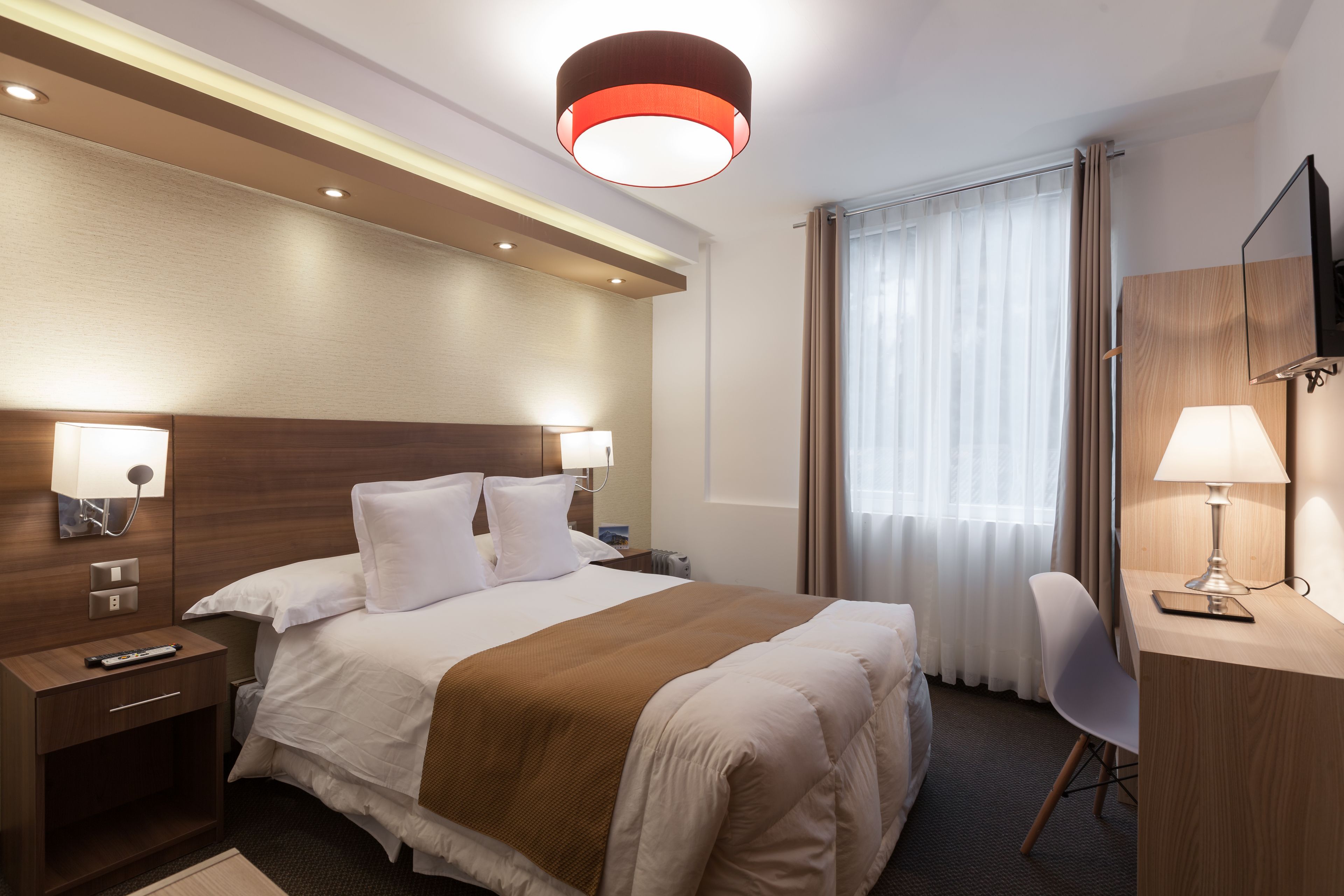 A hotel room with a large bed, bedside lamps, a desk with a chair, and a television.