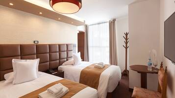 Habitación de hotel con dos camas, un cabecero de madera, una mesita con una silla y un televisor grande en la pared.