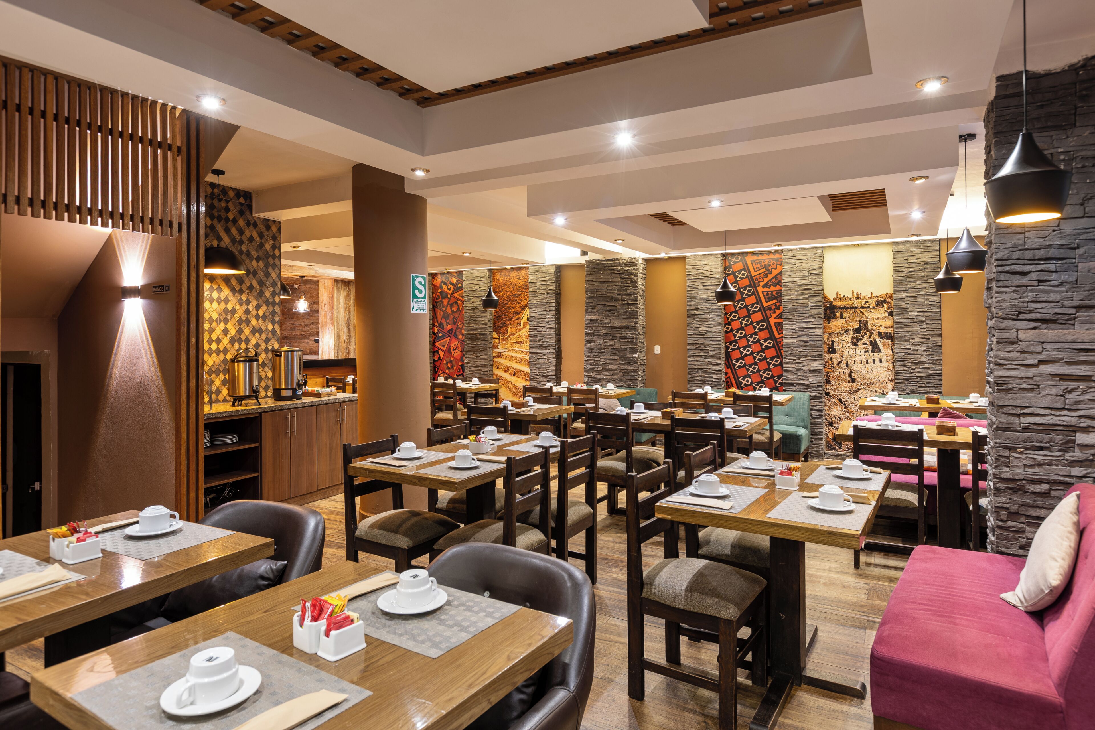 Un restaurante con varias mesas y sillas, una zona de cocina y una pared de piedra con un mural.