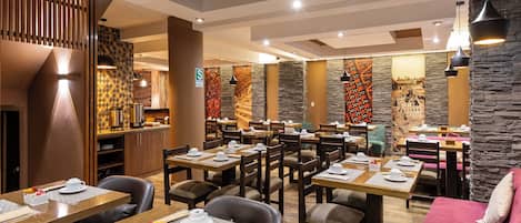 Un restaurante con varias mesas y sillas, una zona de cocina y una pared de piedra con un mural.