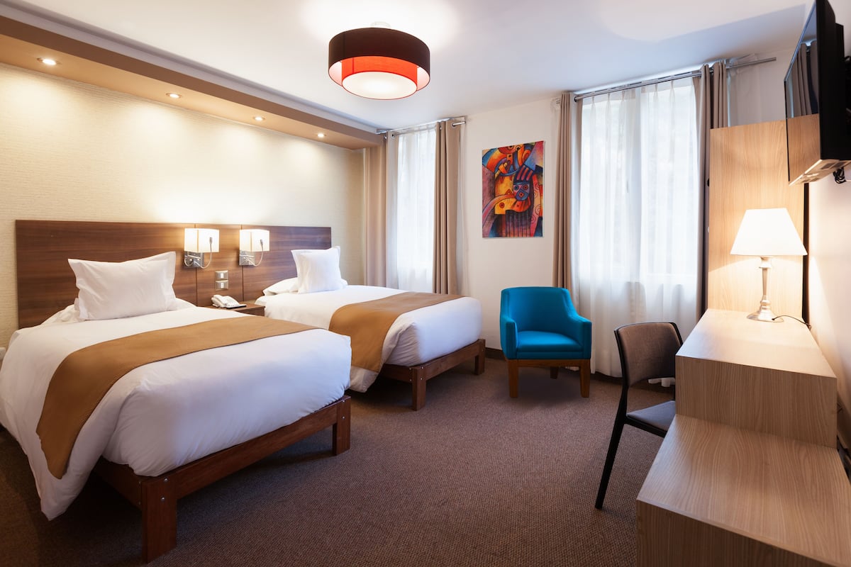 Ein Hotelzimmer mit zwei Betten, einem Schreibtisch, einem Stuhl und einem Fernseher.