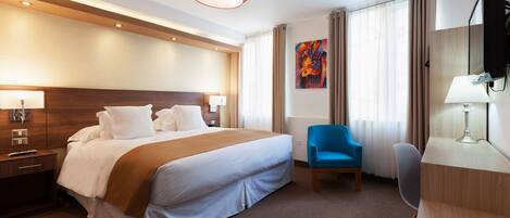 A hotel room with a large bed, a desk, a chair, a TV, and a painting on the wall.