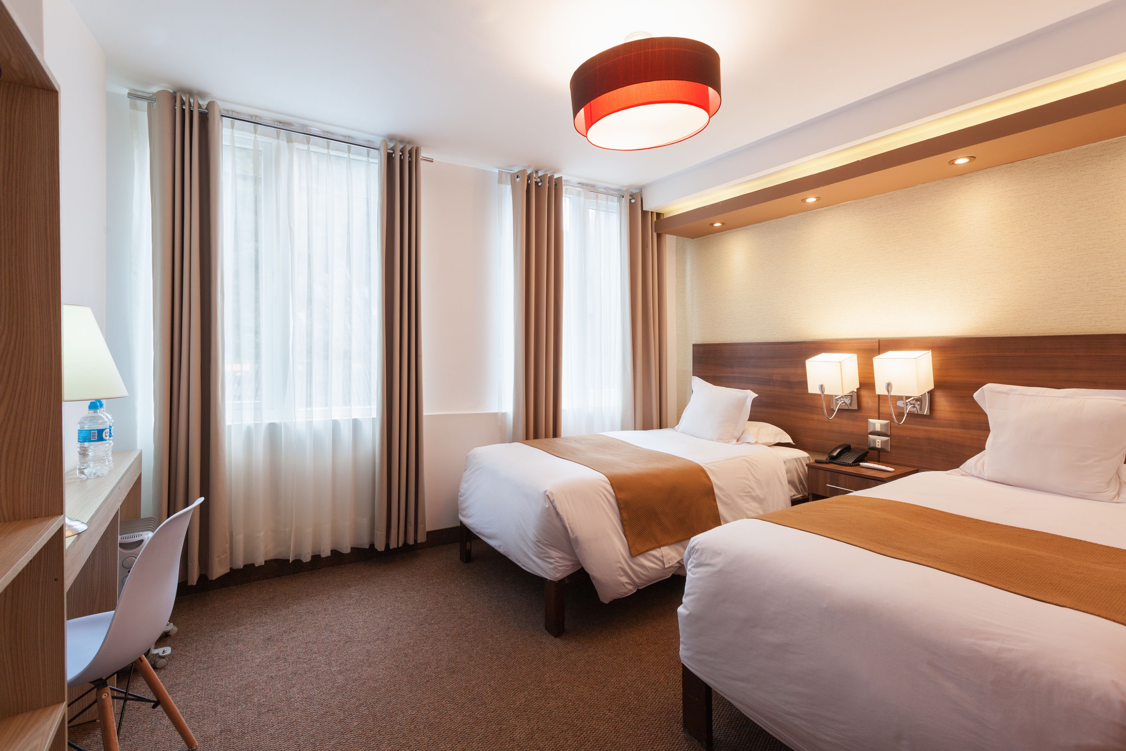 Habitación de hotel con dos camas, un escritorio con silla, una lámpara y un teléfono.