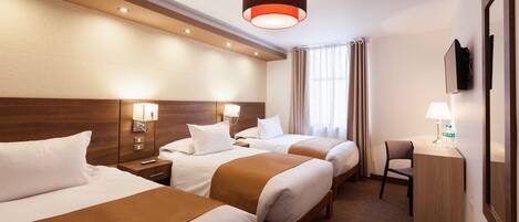 A hotel room with three beds, a desk, a chair, and a TV mounted on the wall.