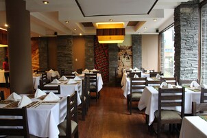 Un restaurant avec des tables dressées pour le service, des chaises en bois et un mur de pierre en arrière-plan.