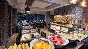 Un buffet proposant une variété de fruits et de boissons, des tables en bois et un mur décoré de motifs.