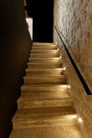 Uma escadaria com paredes de pedra e corrimão, iluminada por pequenas luzes.