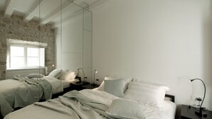 A bedroom with two beds, a large mirror, and a stone wall. - Apartments Eleganca (Dubrovnik)