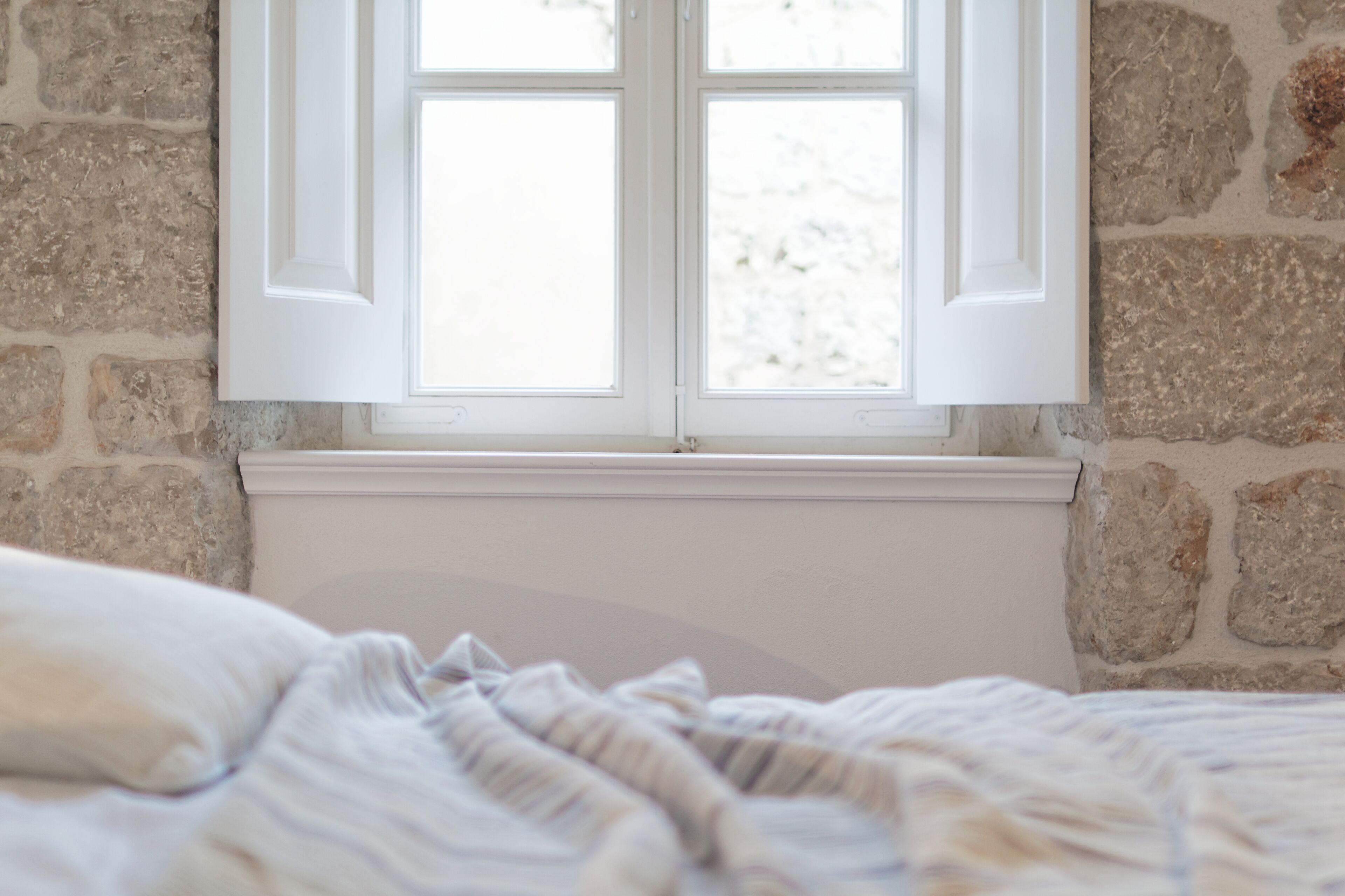 A room with a stone wall, a window with white shutters, and a bed with a striped blanket.