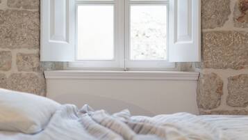 A room with a stone wall, a window with white shutters, and a bed with a striped blanket.