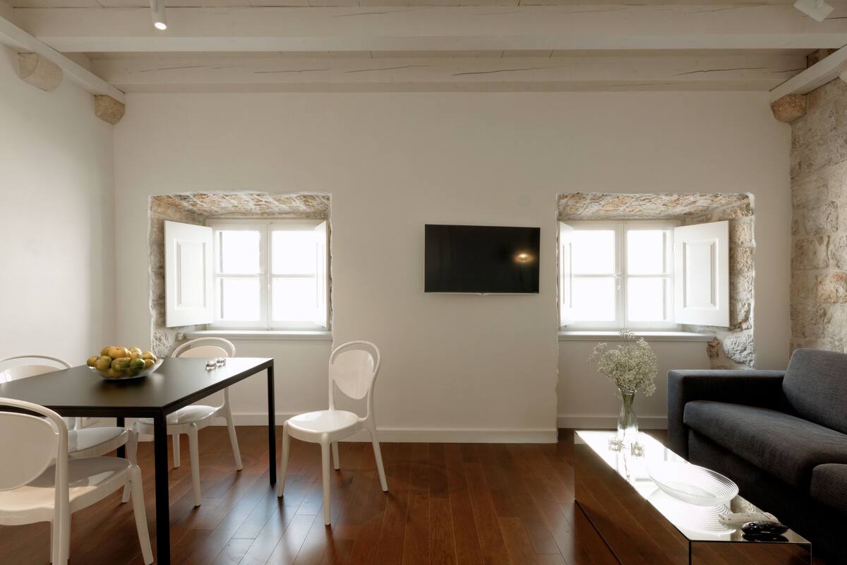 A dining area with a table and chairs, a sofa, and a TV on the wall.
