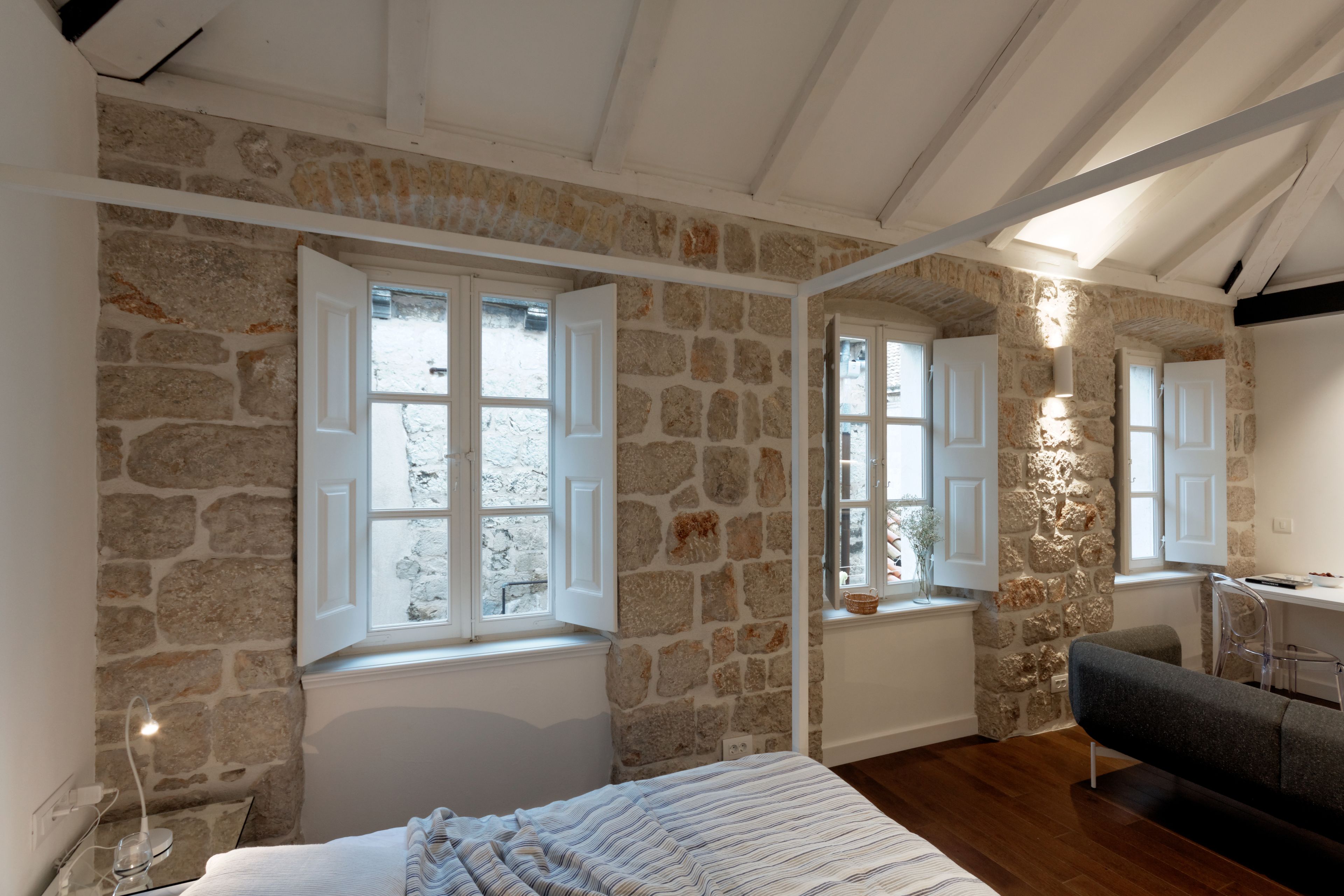 A bedroom with stone walls, a bed, a desk, and a chair.