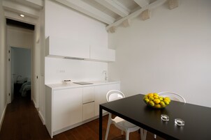 Cozinha moderna com armários brancos, bancada preta e uma tigela de frutas sobre a mesa.