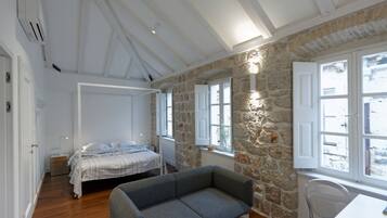 A bedroom with a bed, a grey sofa, stone walls, and large windows.